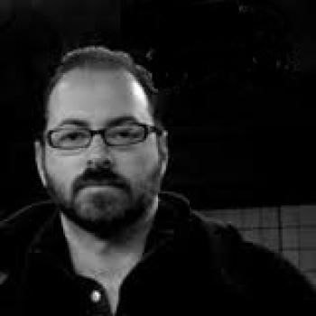 A black and white image of a man with glasses and a black shirt.