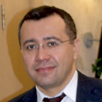 A man in glasses and a maroon tie looks directly at the camera.