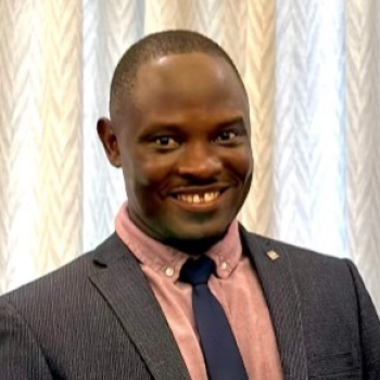 A man in a grey suit and blue tie smiles and looks at the camera.