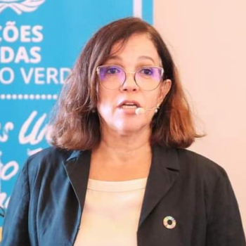 women in black blazer speaks in front of blue banner 