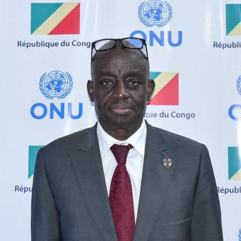 man in grey suit and red tie looks at camera 