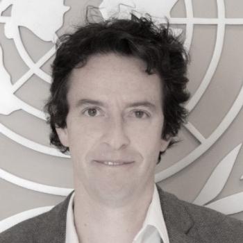 black and white photo of man in suit standing in front of UN logo 