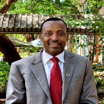 man in grey suit and red tie smiles to camera