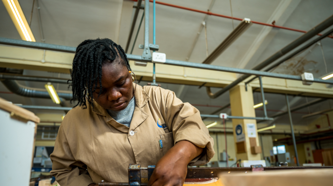 young woman in beige overalls works at a carpentry workshop