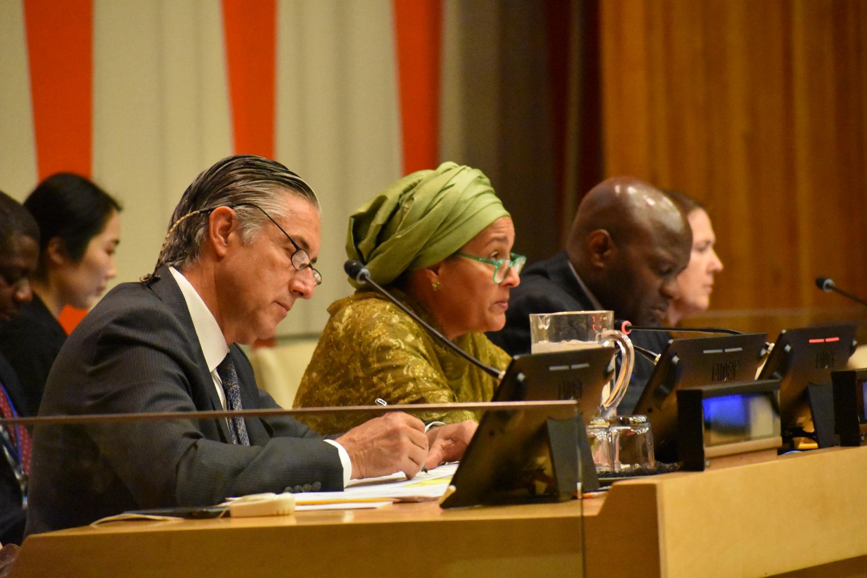 man in suit sits next to woman in green top and head scarf in a panel discussion 