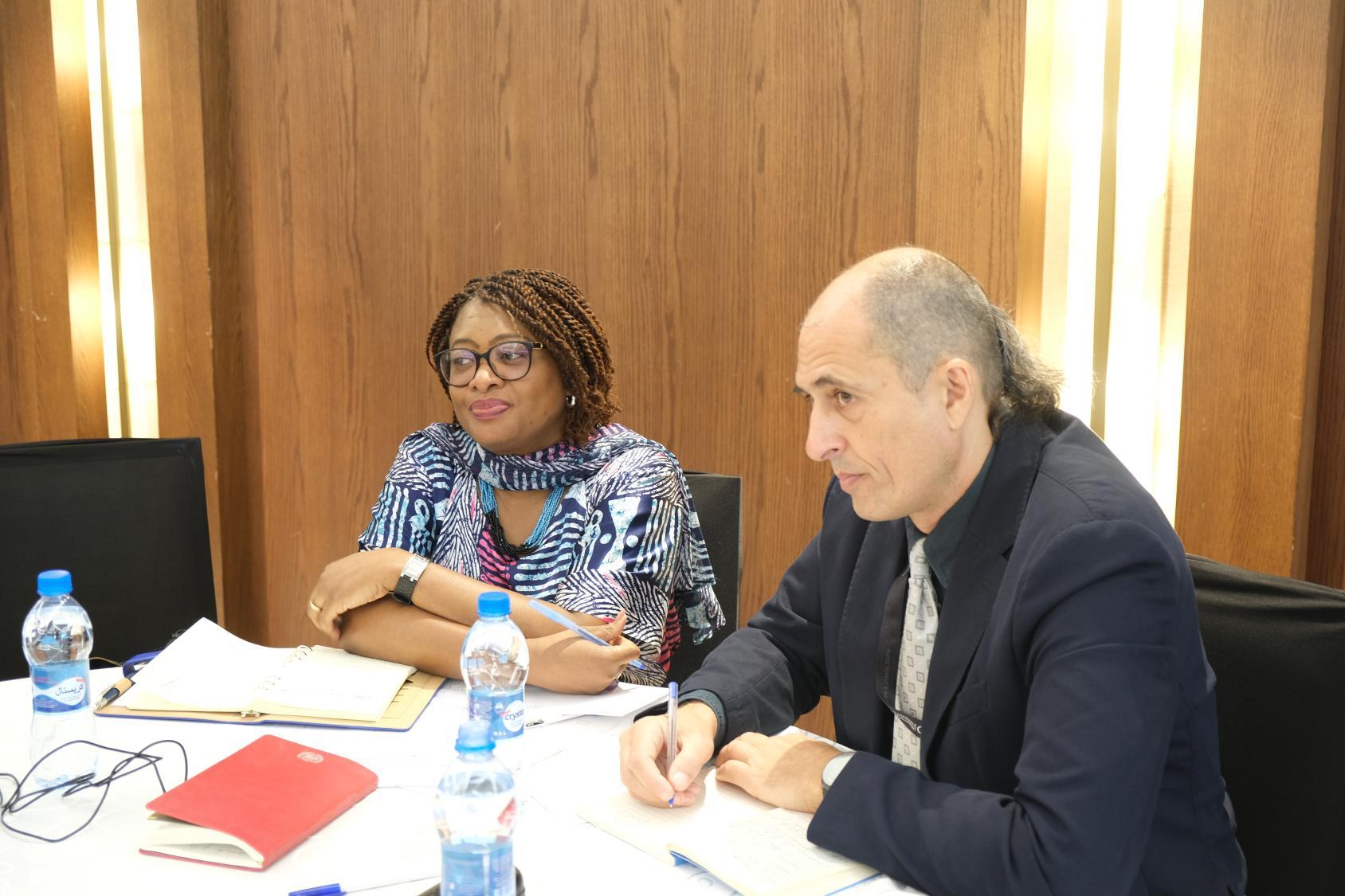 A man in a black suite listens to a discussion with a woman wearing a blue jacket