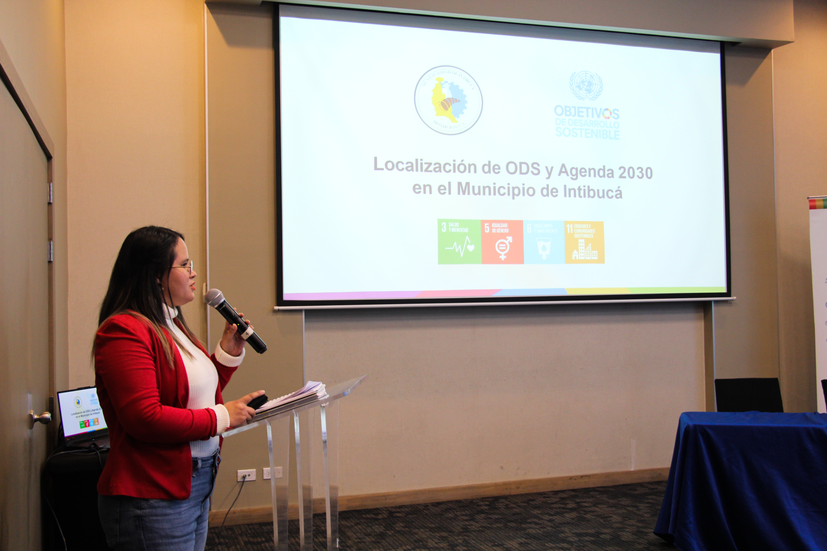 A woman stands in front of a screen explaining to an audience 