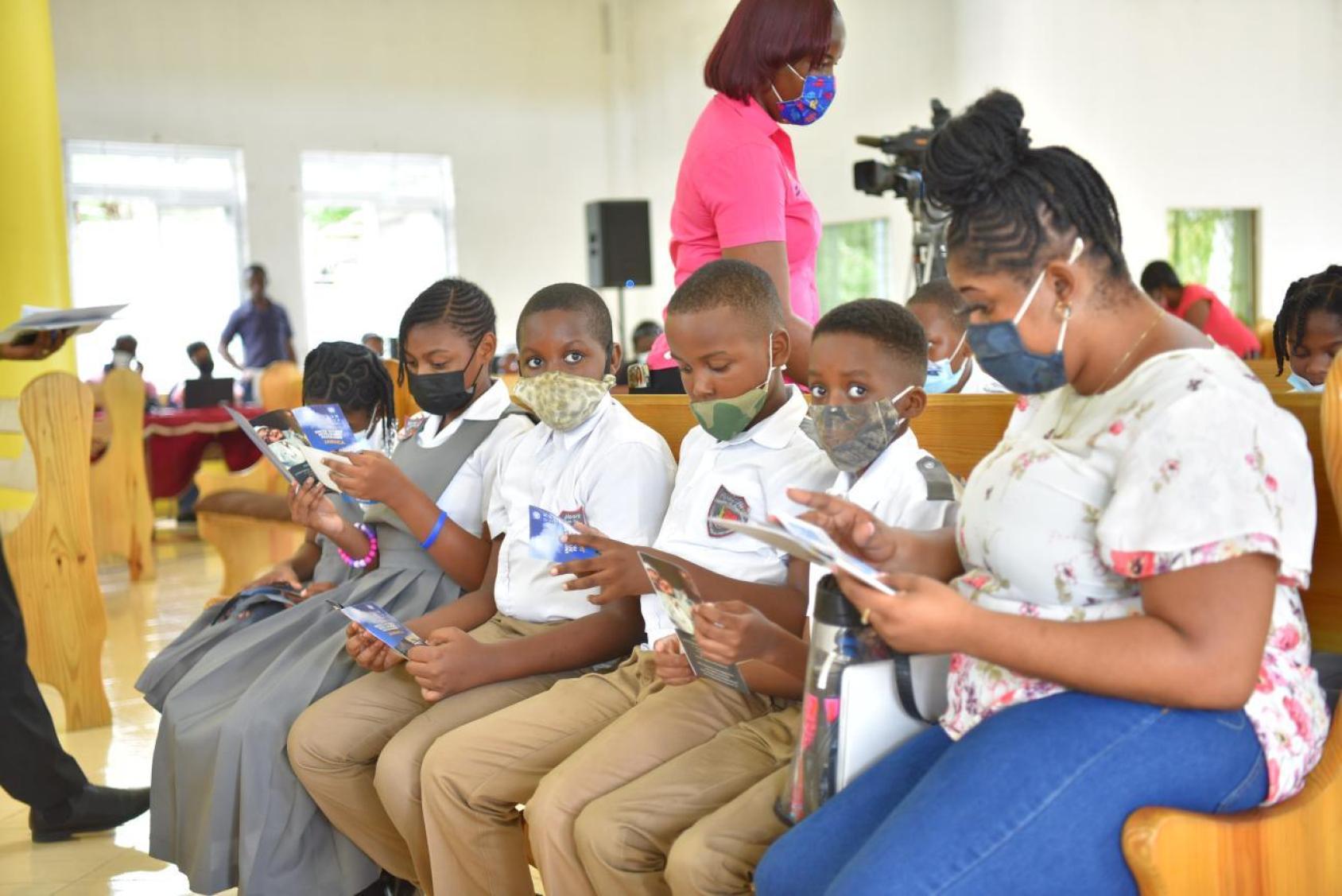 A group of children are looking at leaflets and seated next to a teacher