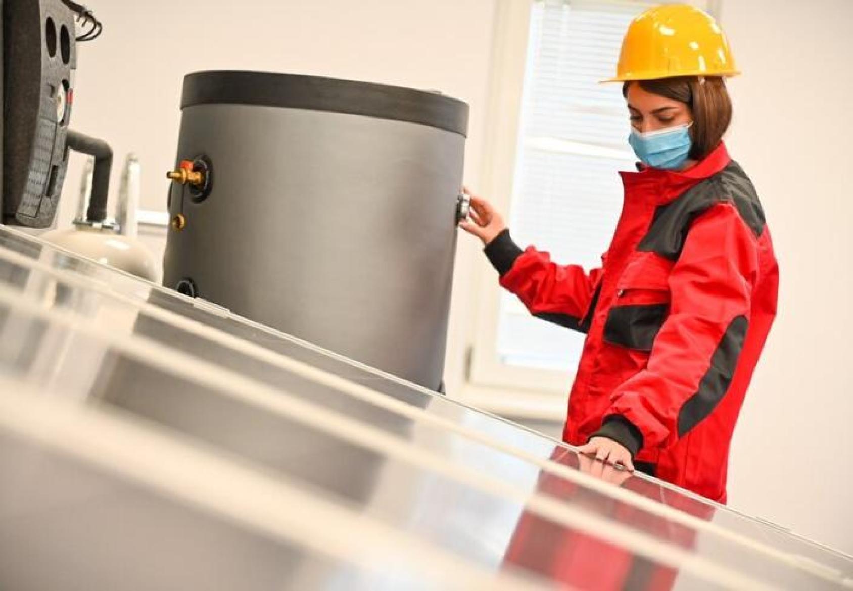 A woman stands next to a boiler