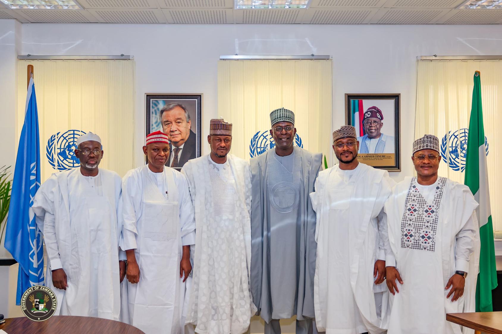 A group of men dressed in traditional African dress, standing in front of flags of the UN and Nigeria