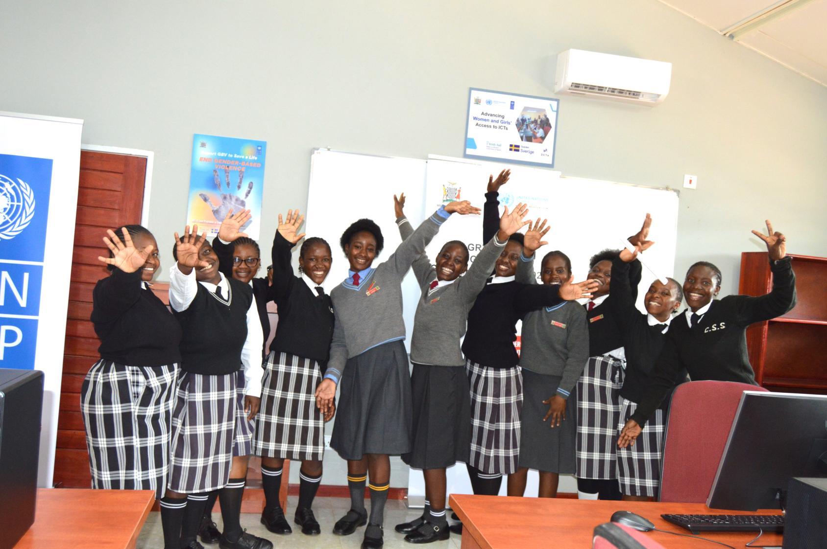 A group of school girls in front of a whiteboard. They are standing in a smart classroom with computers and desks around them