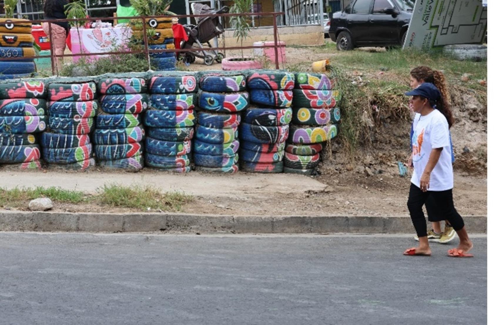 Two women are walking down a street with a colourful tower of tyres