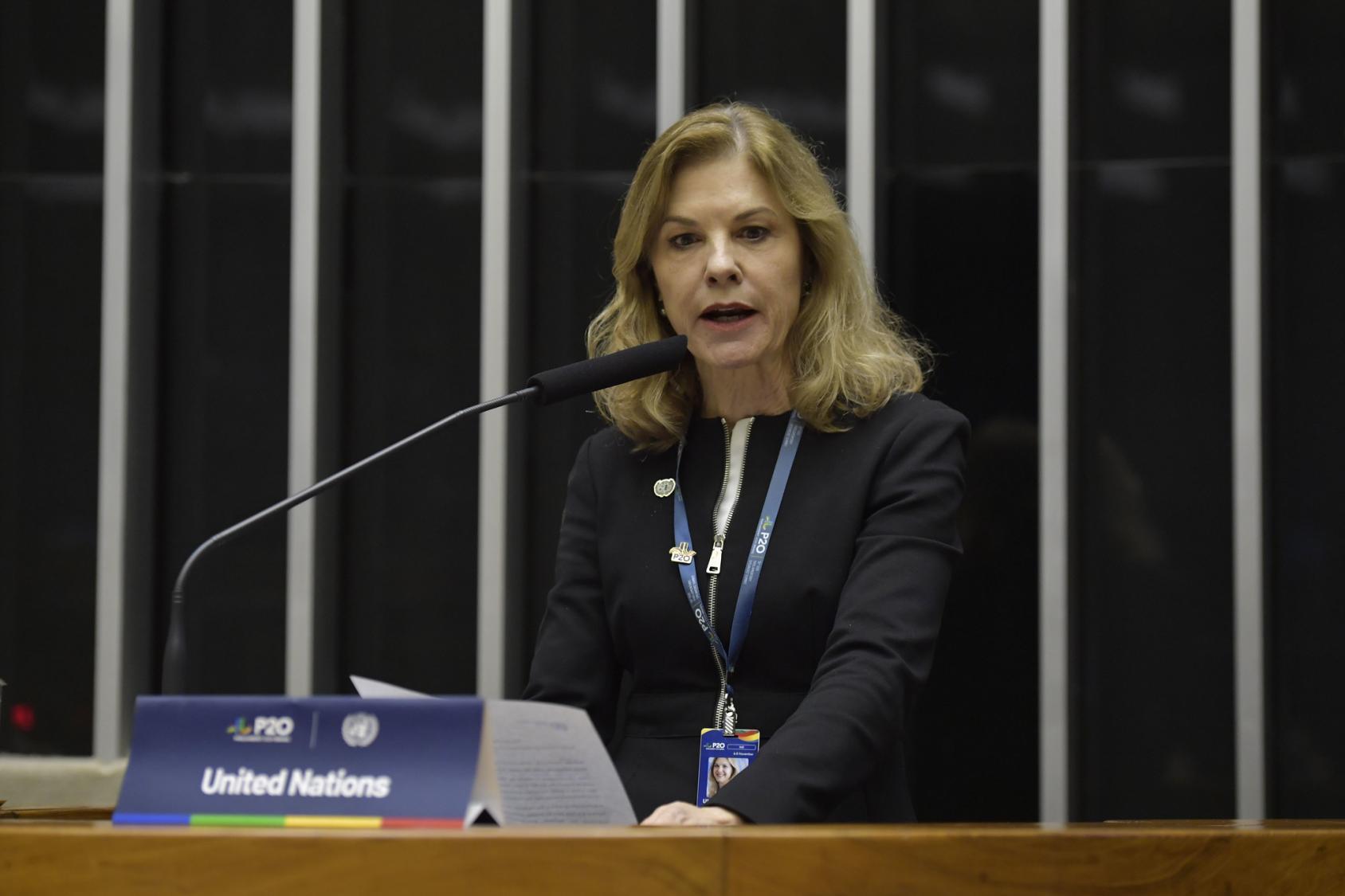 UN Resident Coordinator in Brazil, Silvia Rucks speaking in front of a background with flags of the G20