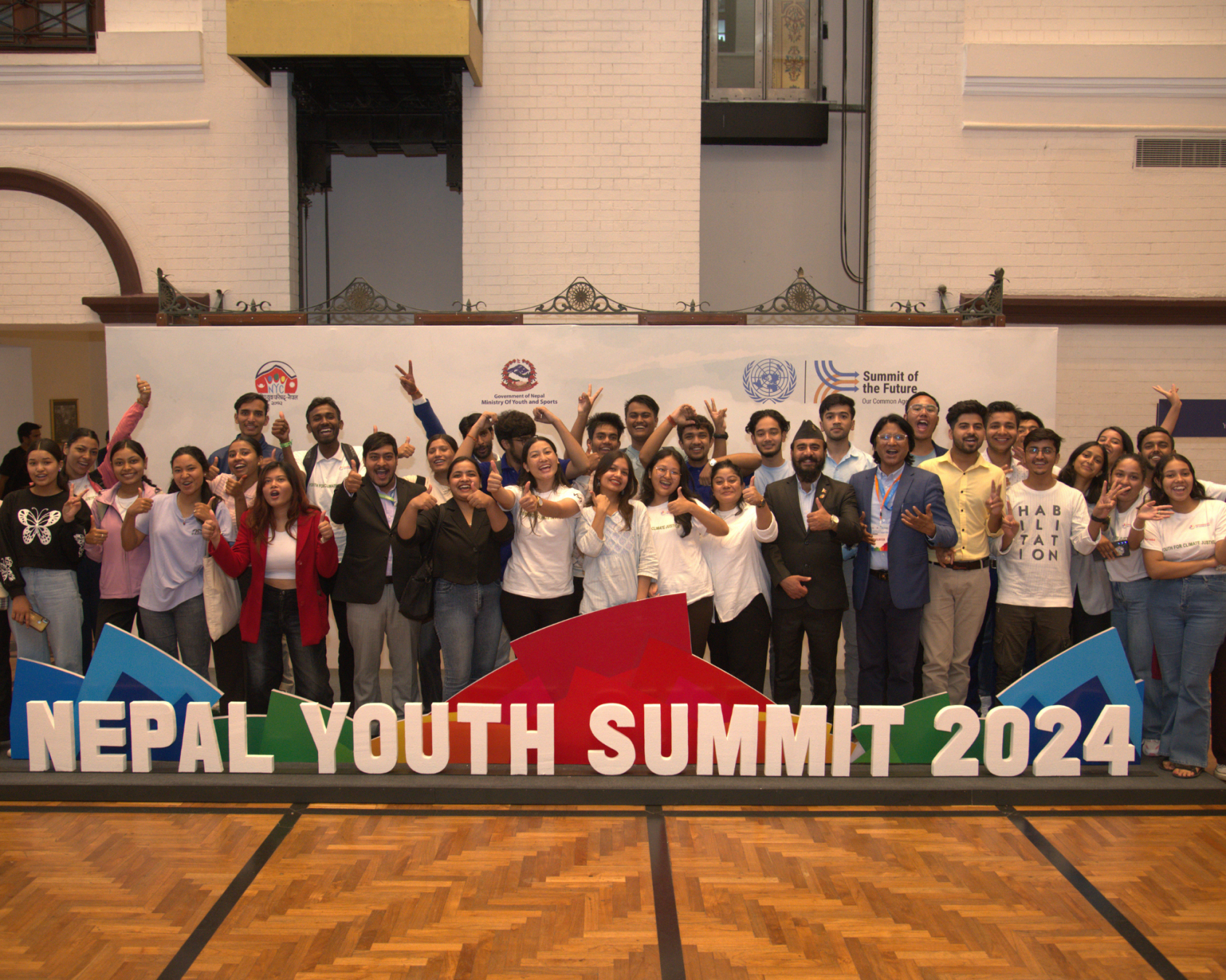 A group of young people, standing behind a sign that reads Nepal Youth Summit