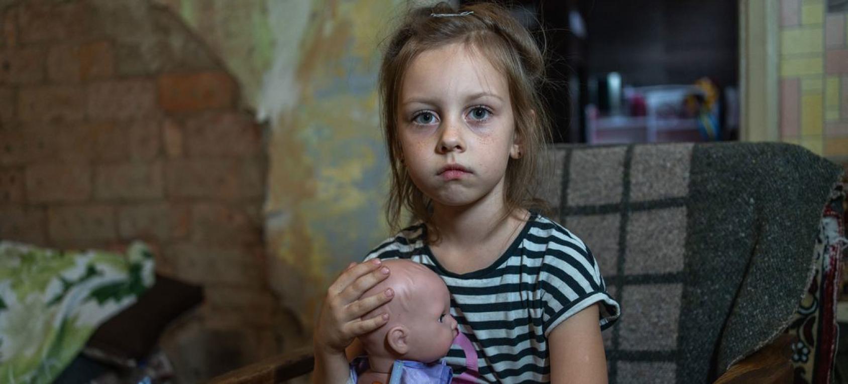 A little girl is holding onto a doll and looking at the camera 