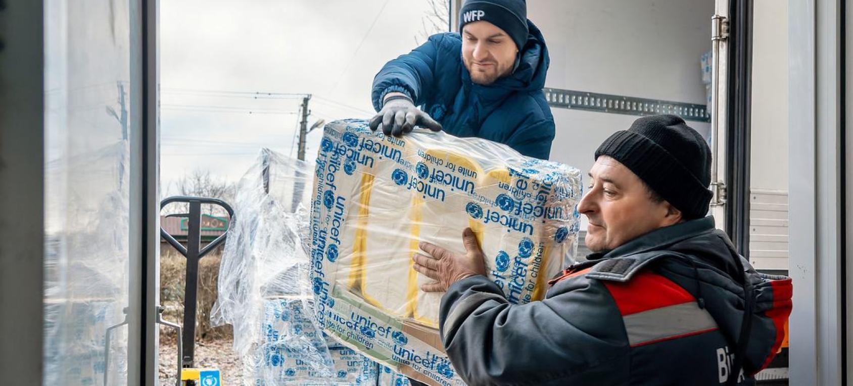 Two men are unloading supplies that have UNICEF branding on them