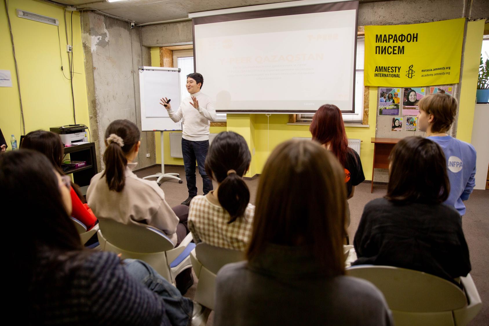A man is in front of a large classroom speaking to students