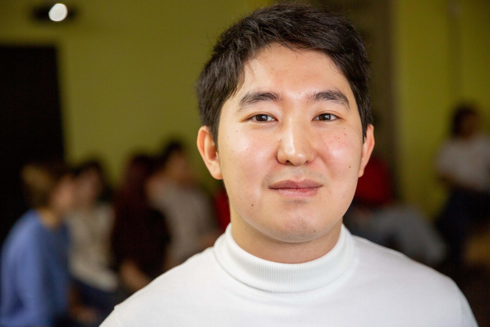 A man looks at the camera and smiles, he is wearing a white top
