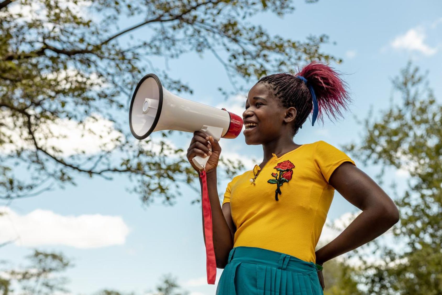 A young woman holding up a megaphone in an outdoor setting