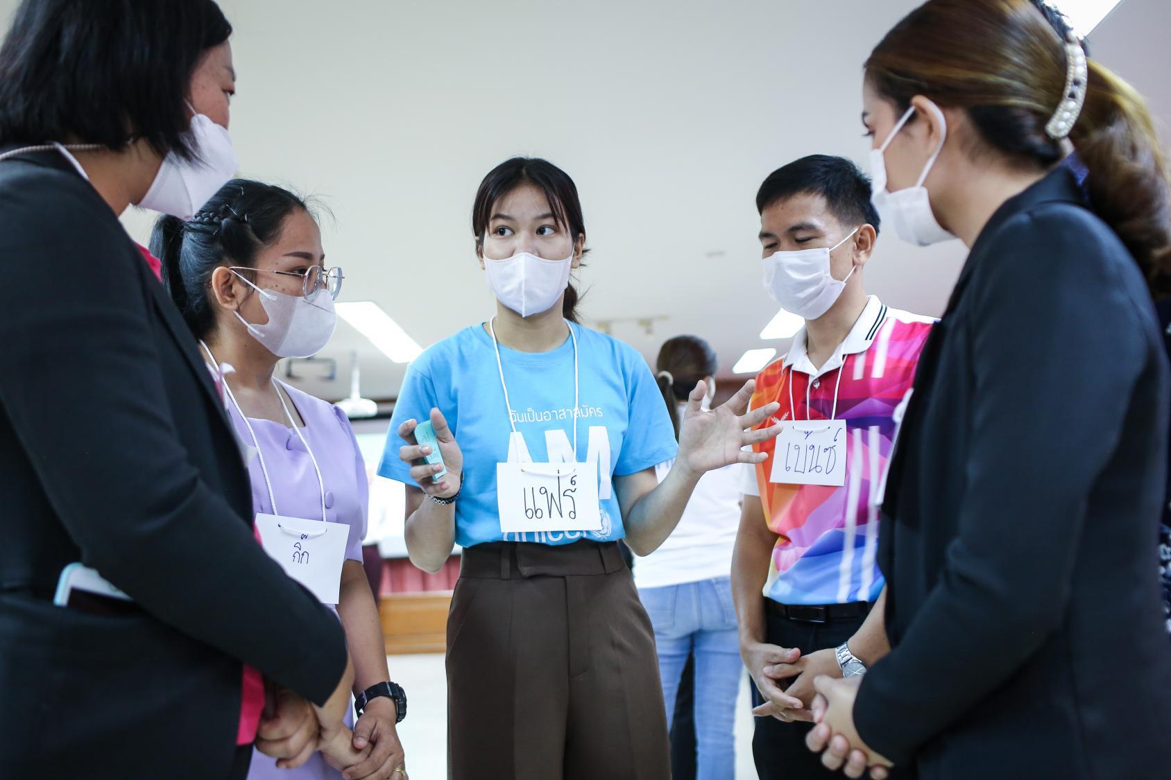 a group of young people in an indoor setting, wearing masks and talking to each other