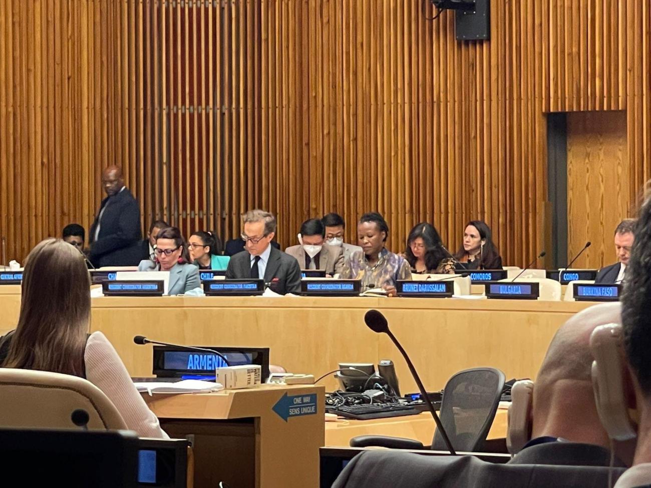 An image of several people in a meeting room with country signs displayed in front of each seat.
