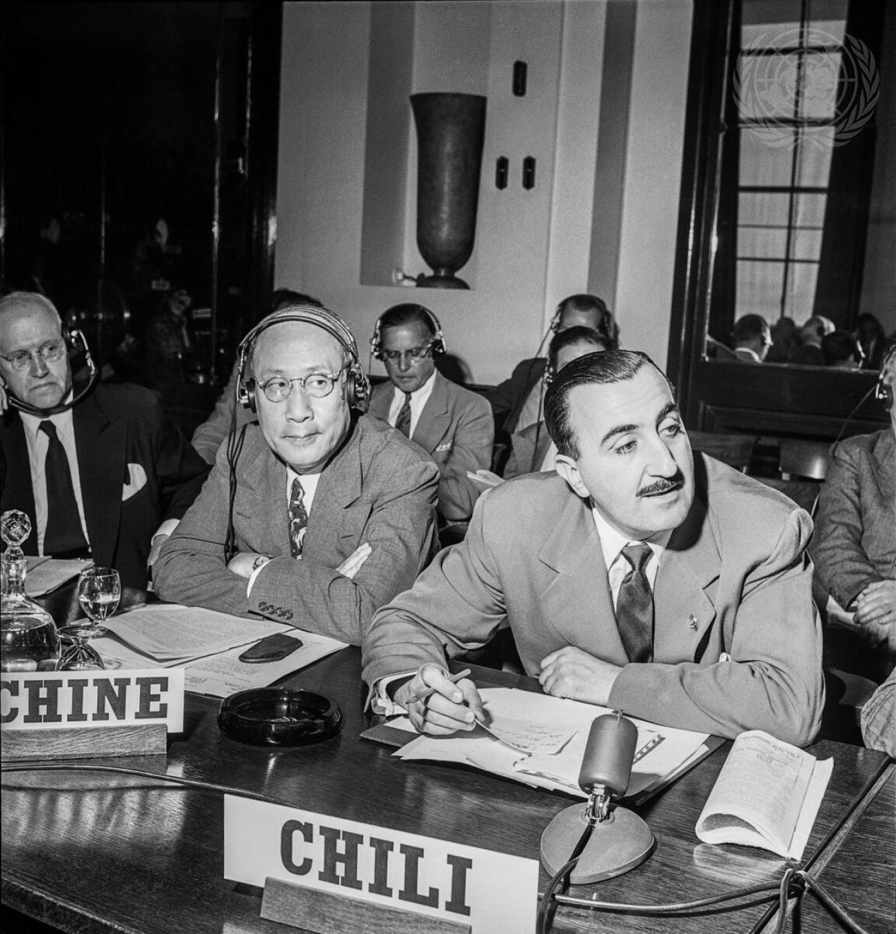 black and white photo of two men sitting at a desk with microphones 