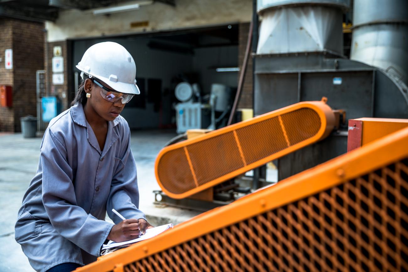 Women in hard hat kneels down to work on machinery 