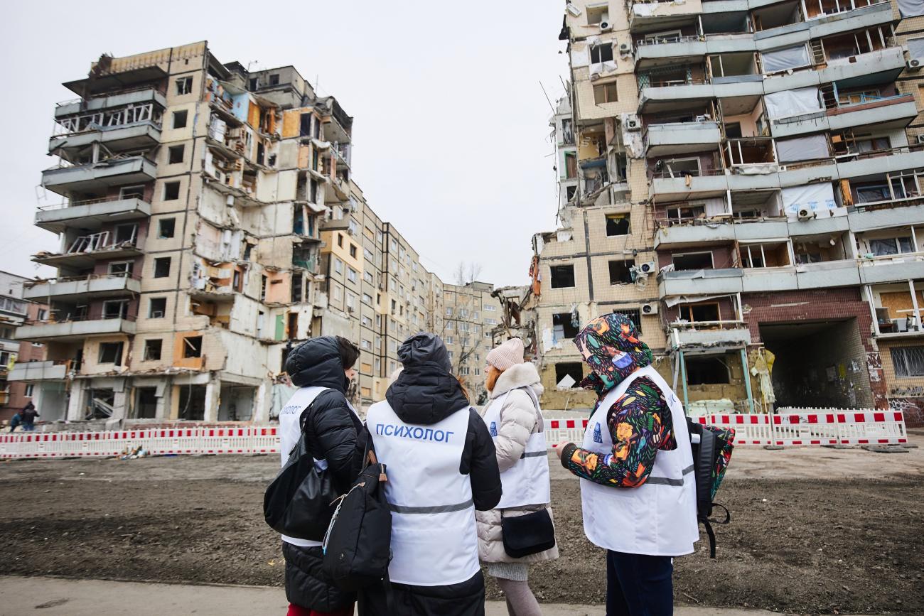 women stand in front of building which has been destroyed