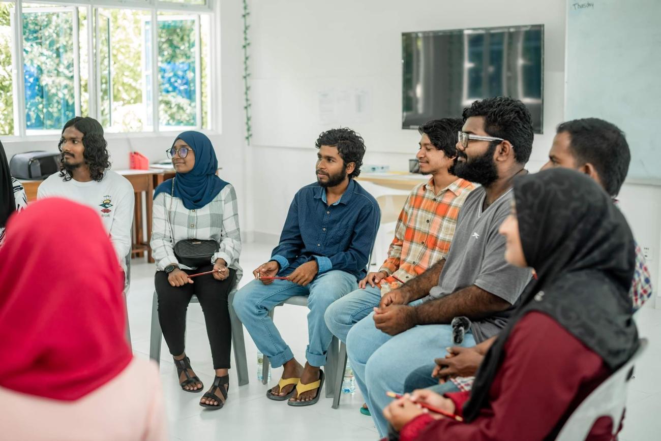 group of young people sit in circle speaking 