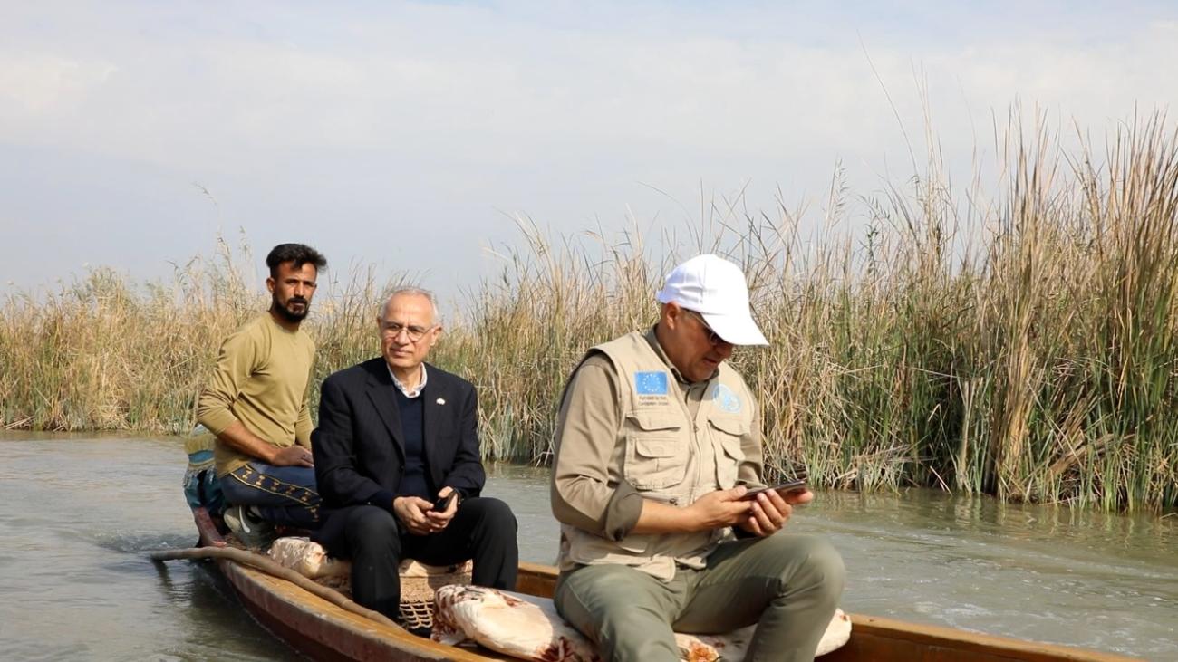 three men sit in a boat going down a marsh river in Iraq