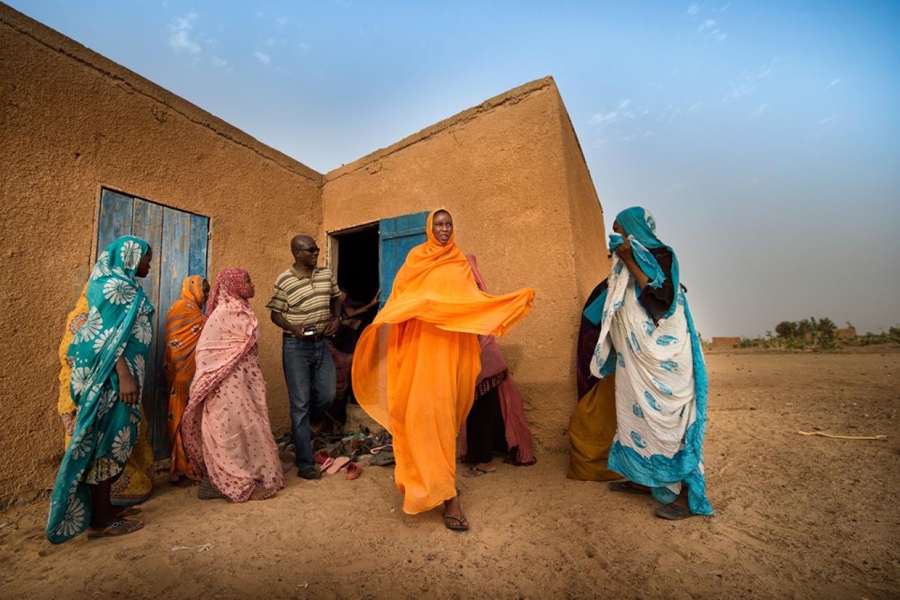 People in colourful clothes stand outside a building