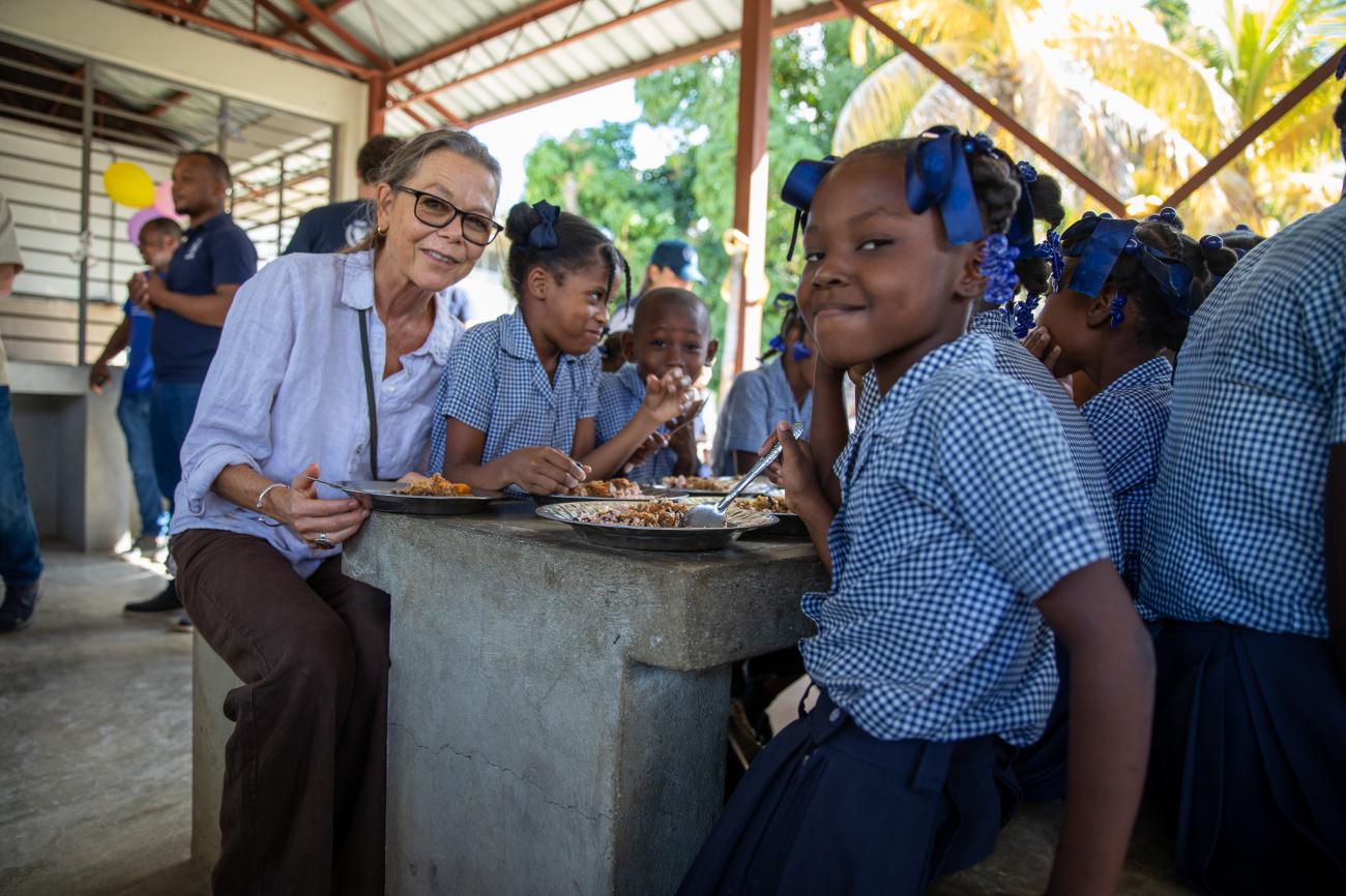 women sits down at a table with school children 