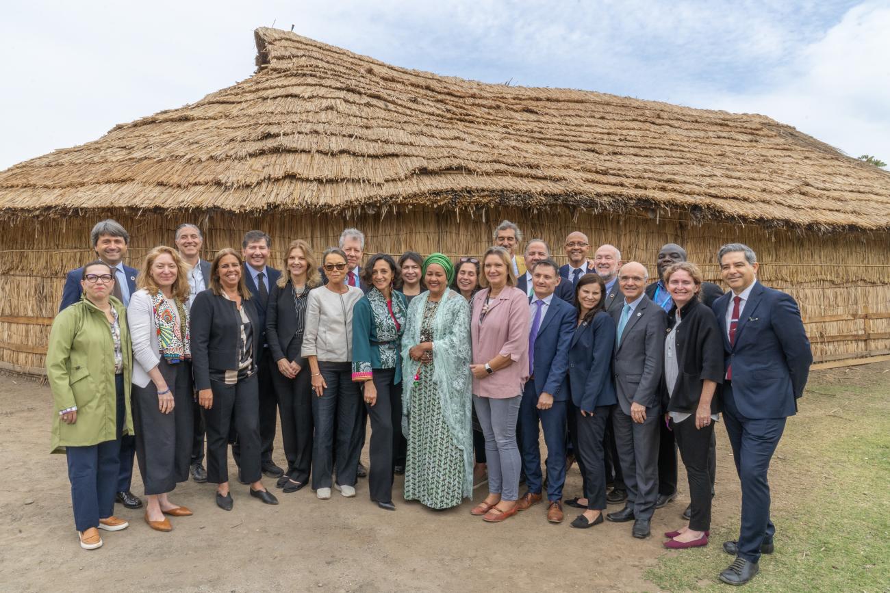 Group of people stand outside house with straw roof 
