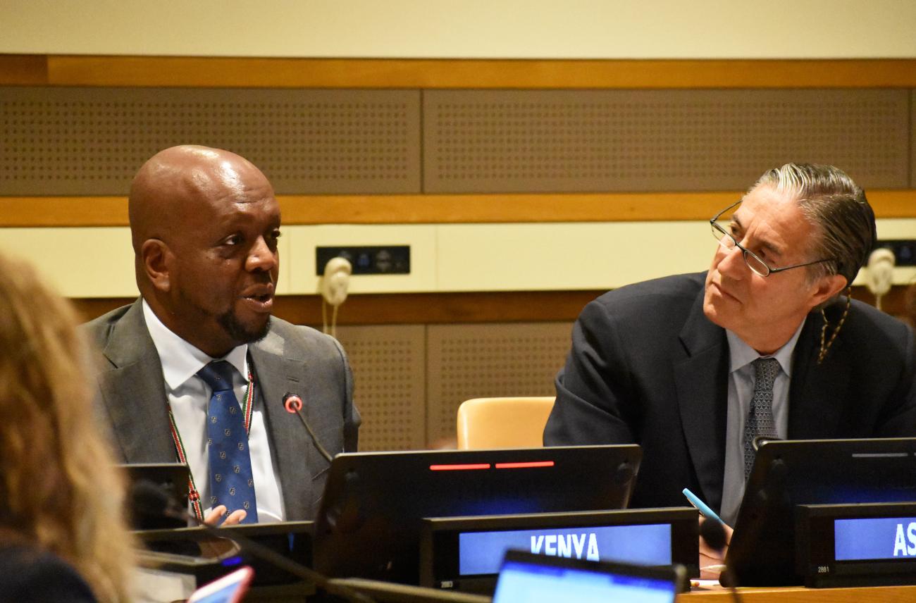 two men in dark suits sit at panel discussion 