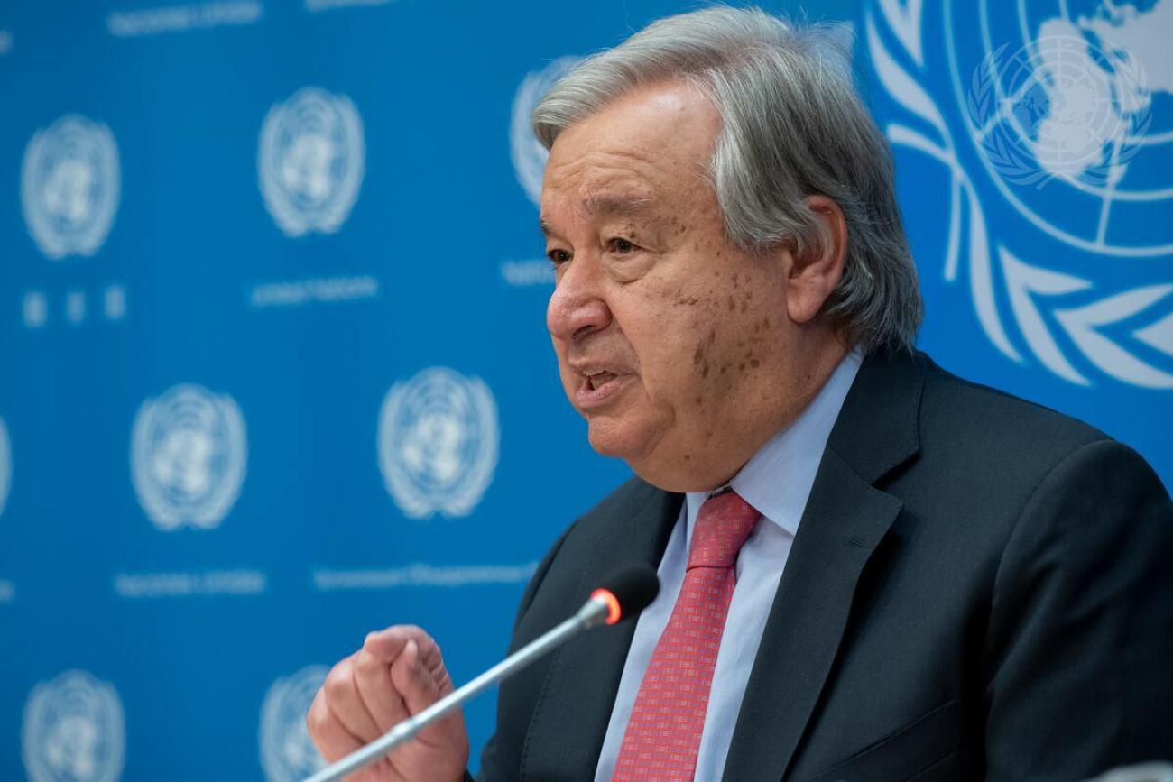 man in dark suit and pink tie speaks into a microphone