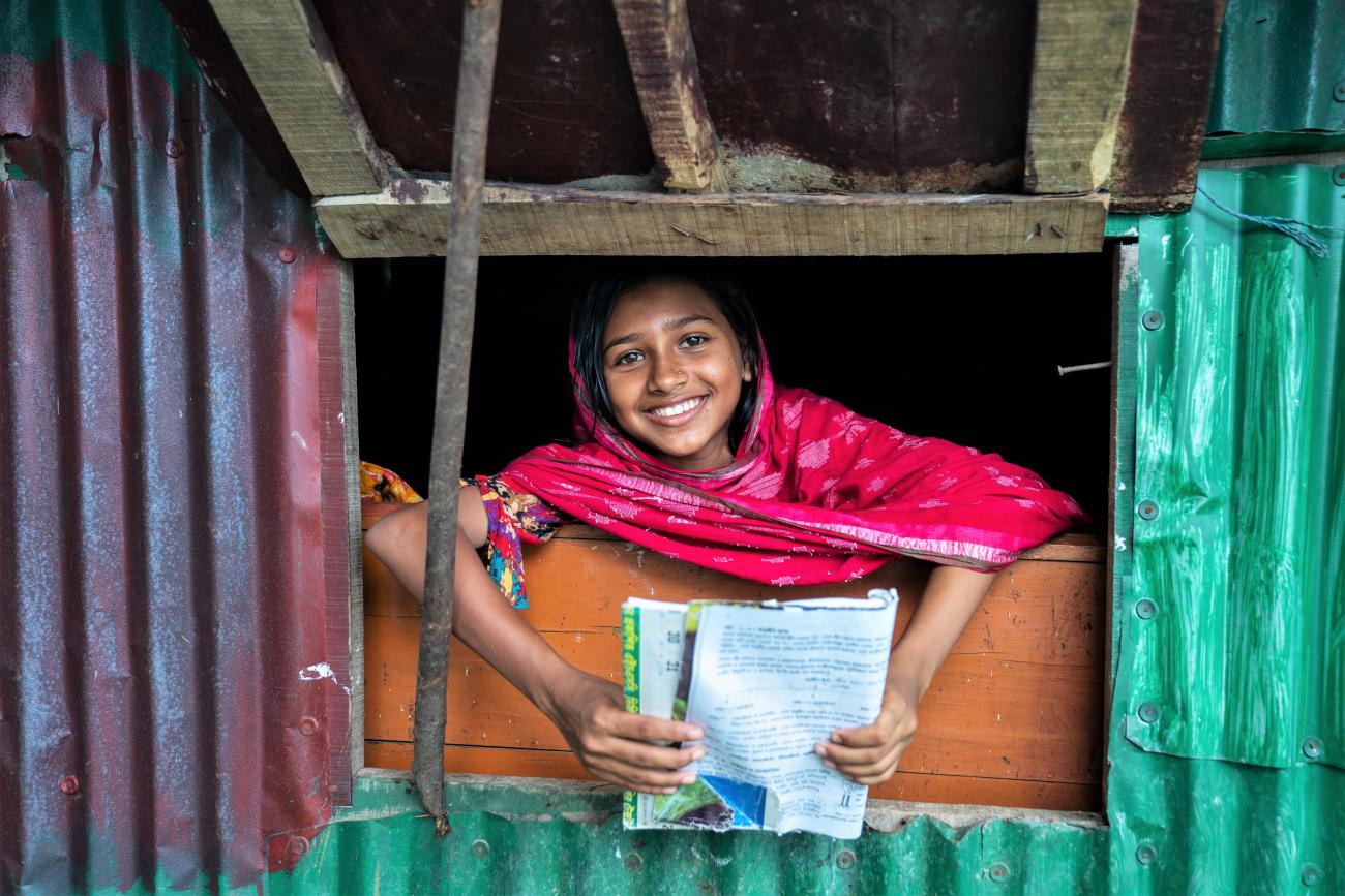 young girl leans outside a window holding piece of paper