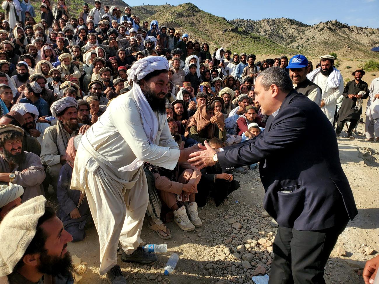 man in dark suit shakes hands with man in white robes 