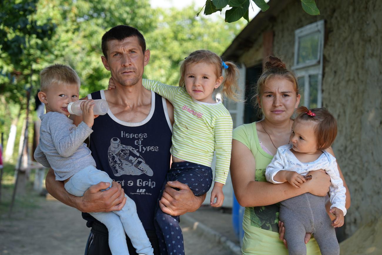 A man and woman stand facing the camera holding their three young children