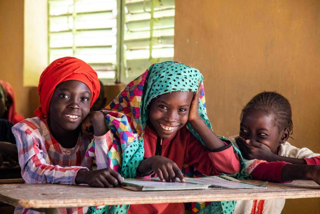 group of three young children sit next to one another and smile at the camera 