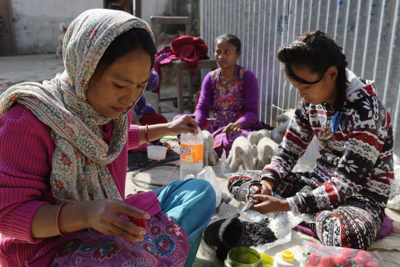 group of people sit down on the ground working with crafts and textiles
