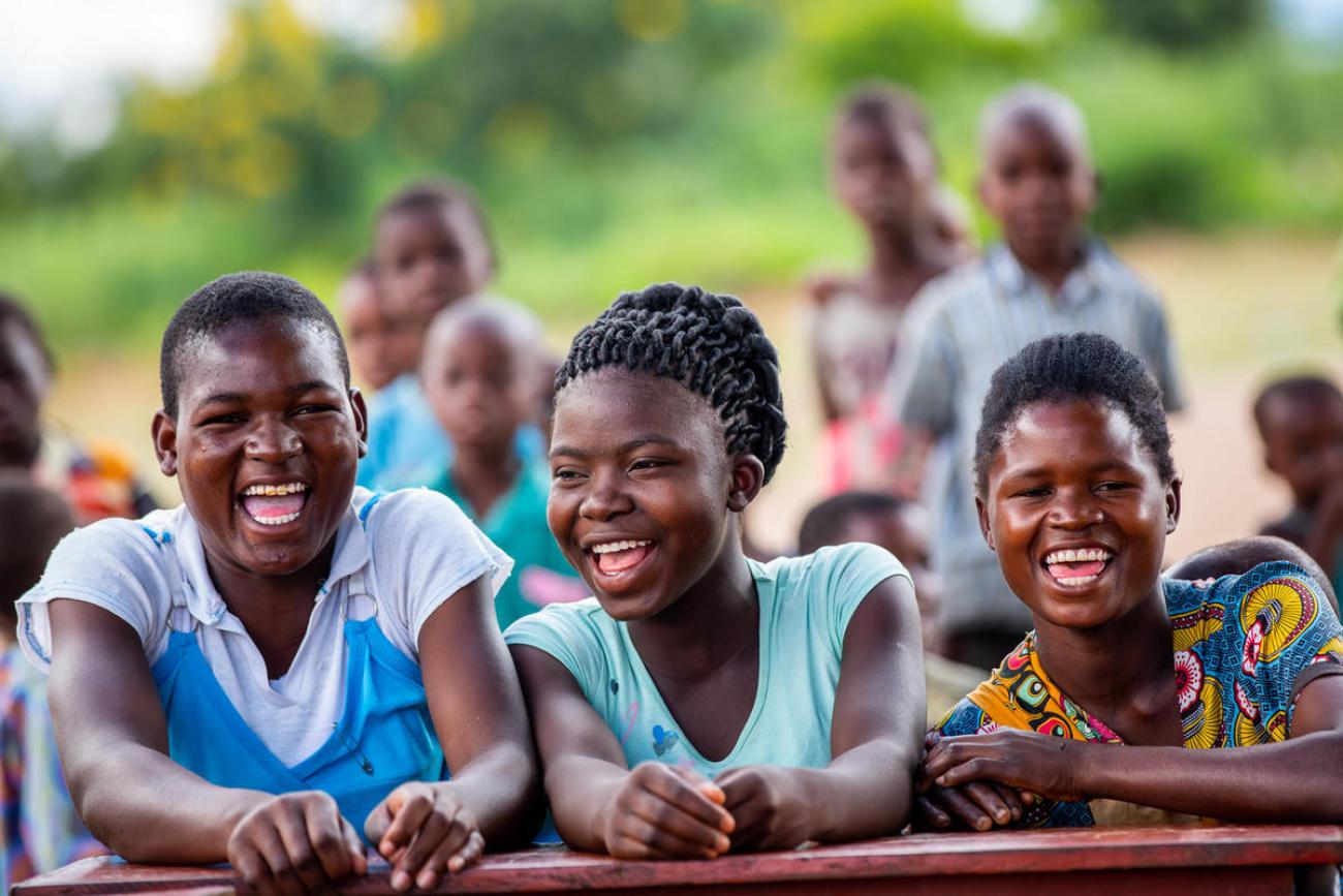 three young people sit together outside laughing and smiling at the camera