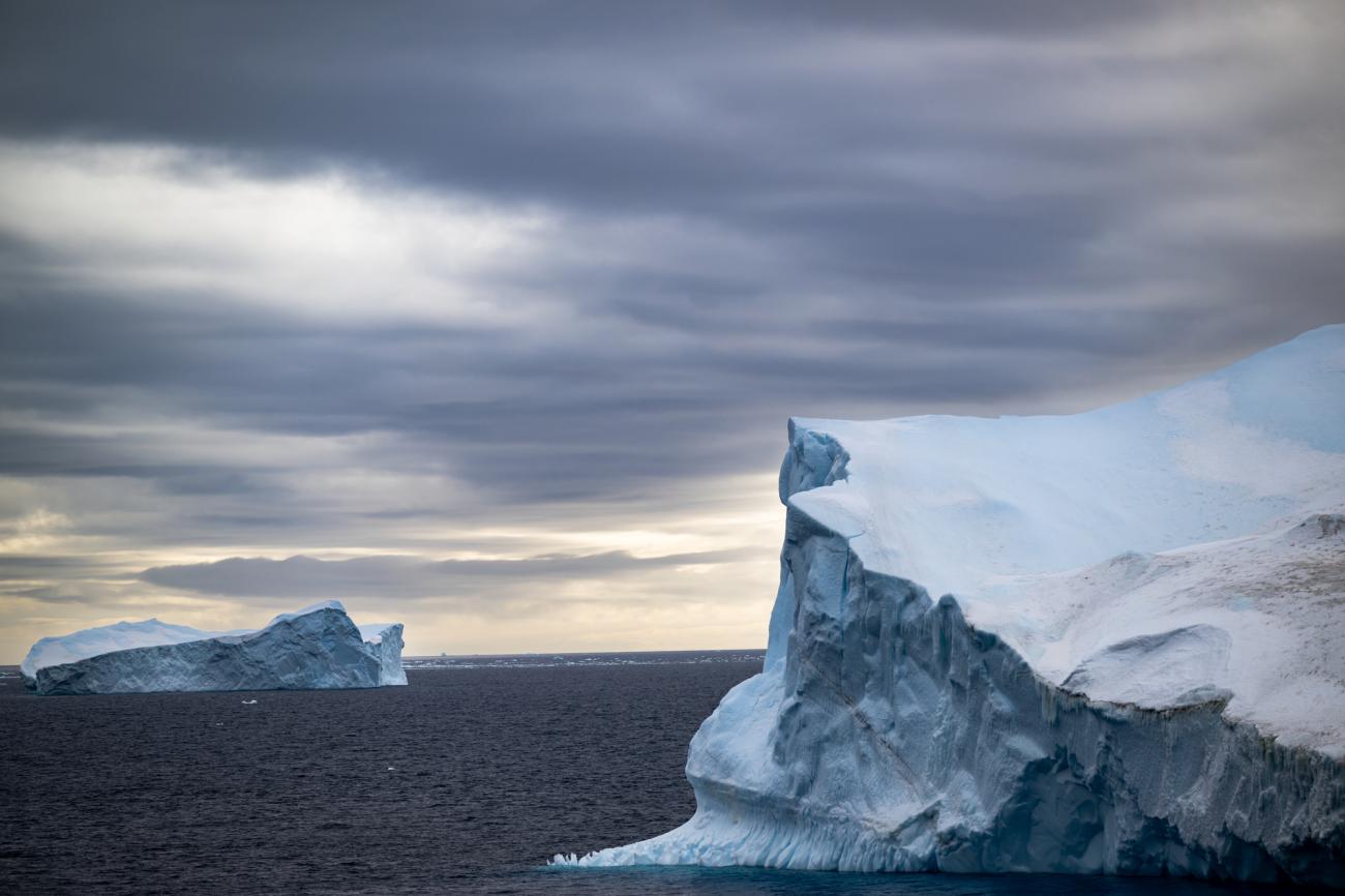 two mountains of ice float in the Antarctic sea against cloudy sky