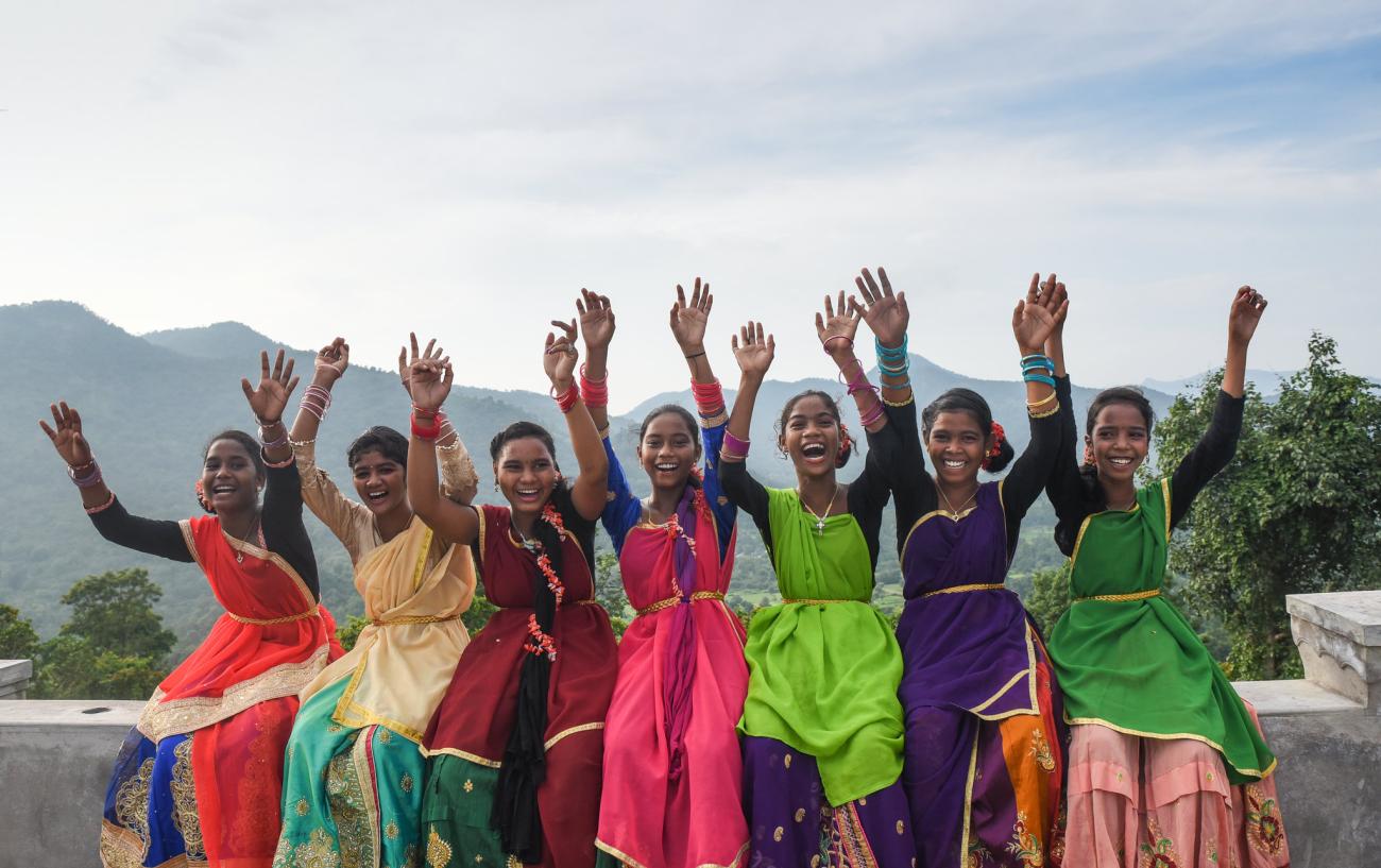 women in colourful saris raise their arms in the air and smile to the camera