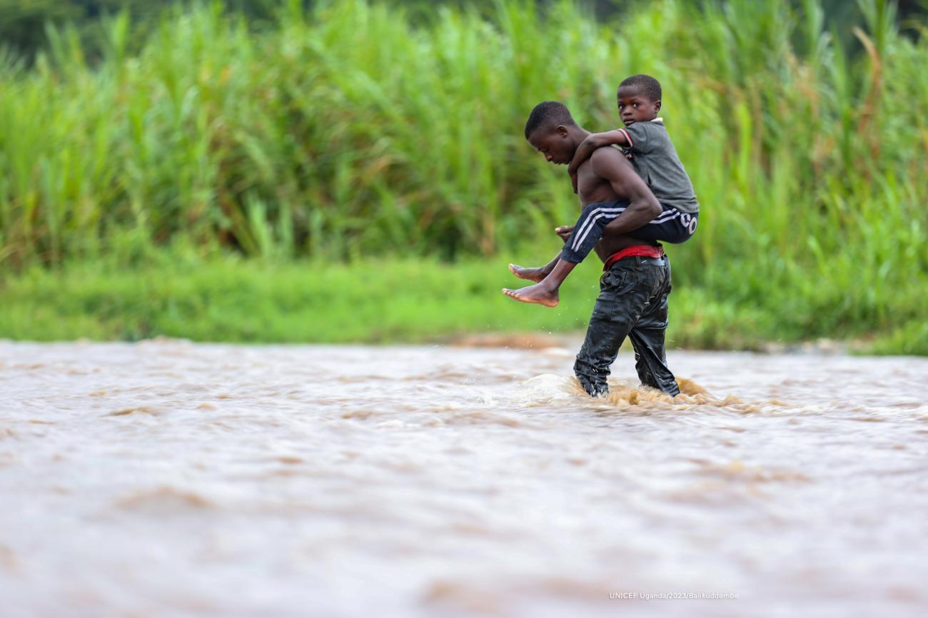 boy carries younger boy on his back as his walks through a river