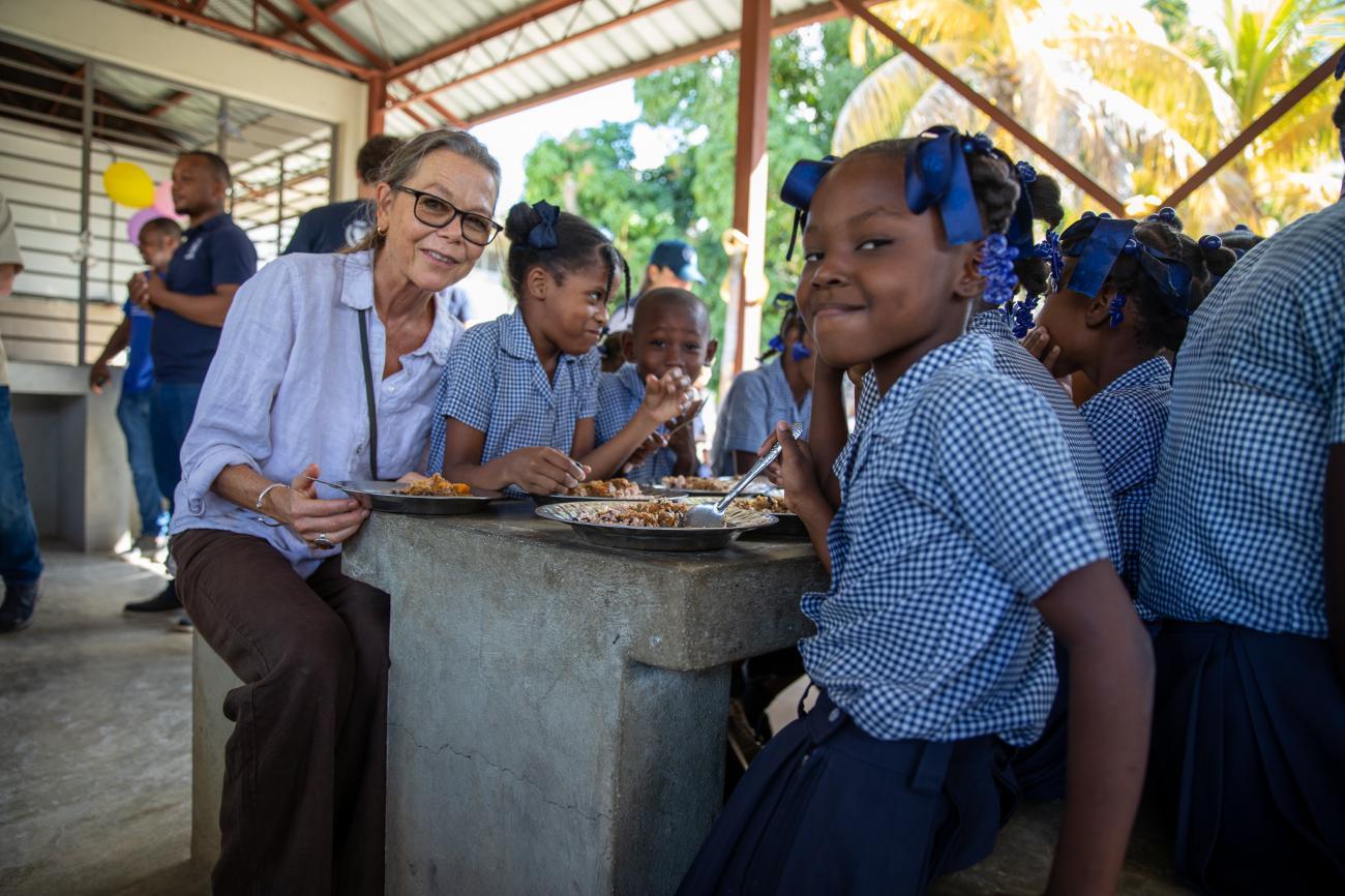 woman sits with school children around a table eating 