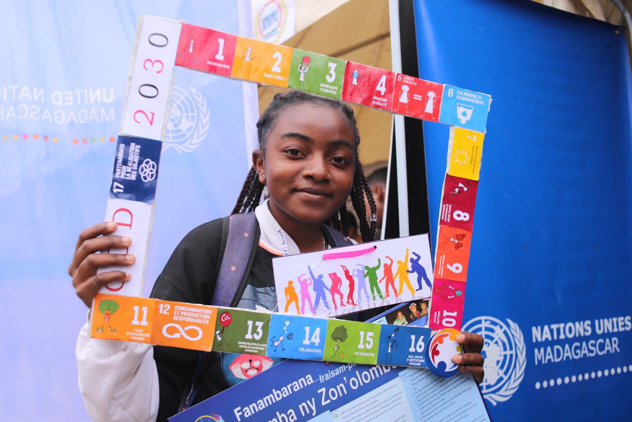 A young girl holds up a banner of the SDGs, she is smiling