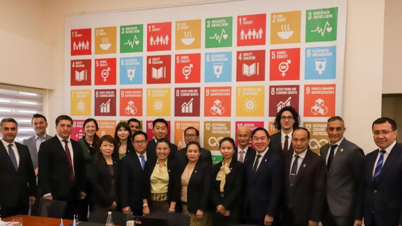 A group of people looking at the camera with the colourful SDG logos in the background 