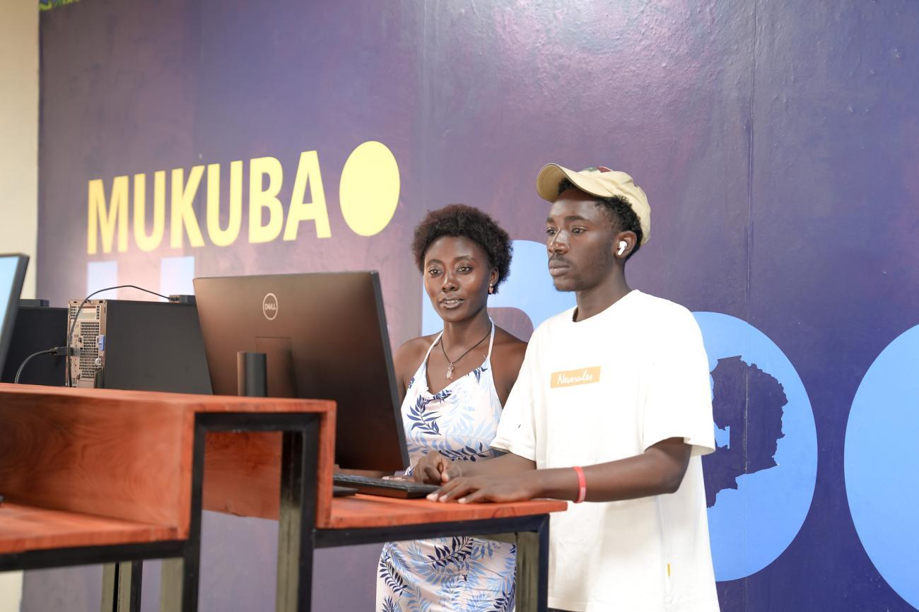 Two people in front of a computer with a colourful background behind them