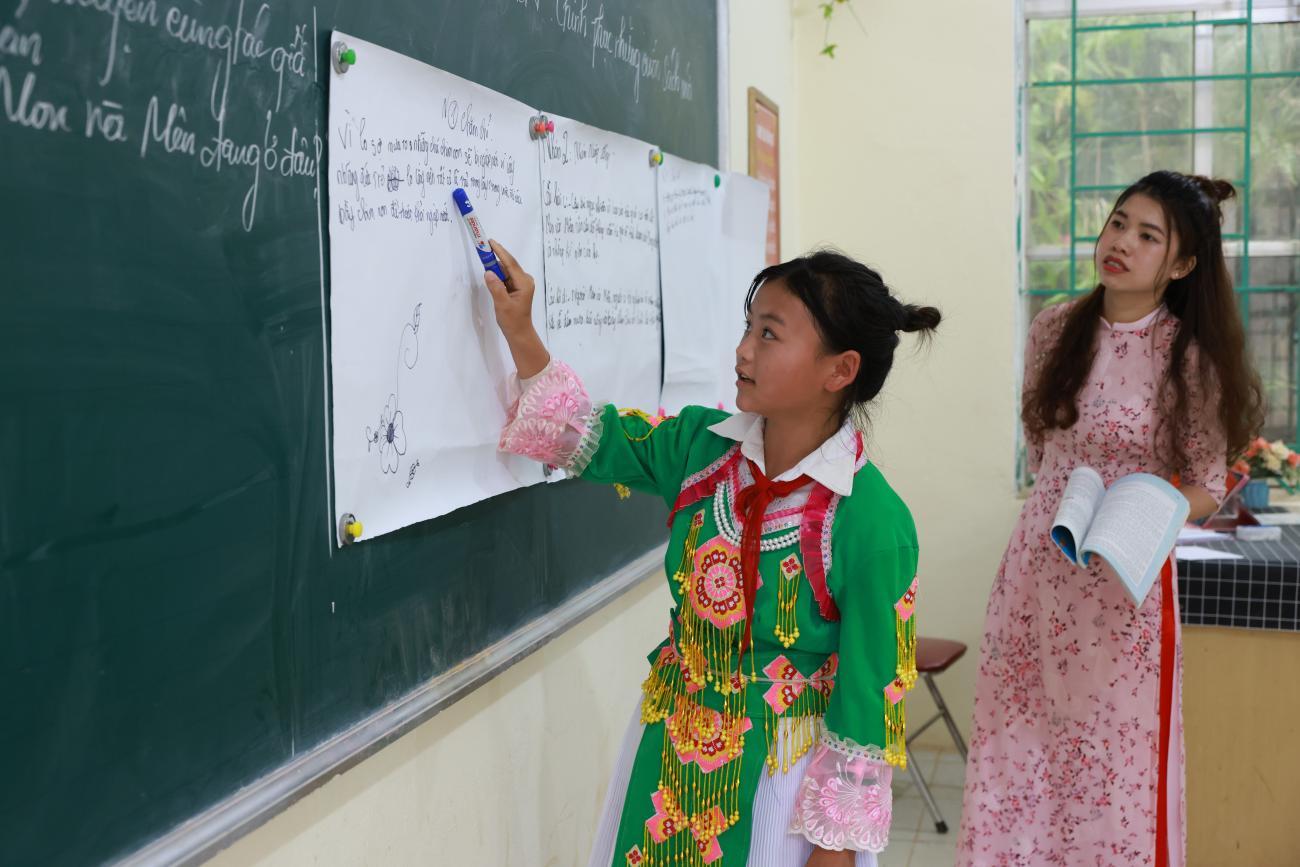 A young girl is writing on a black board in a classroom