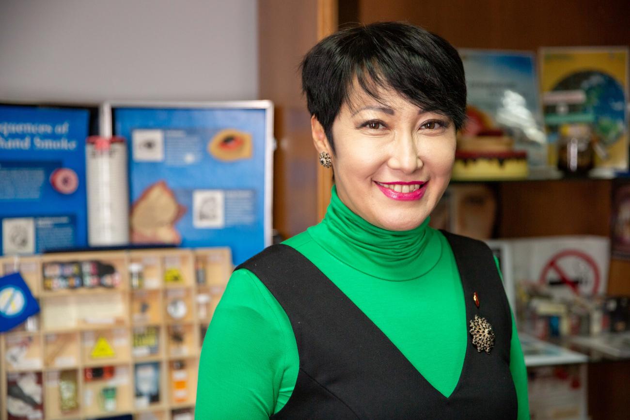 A woman wearing a green top and blue blazer looks at the camera and smiles